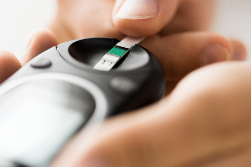 Close-up of a person holding a black glucose meter with a test strip, preparing for a blood sugar test.