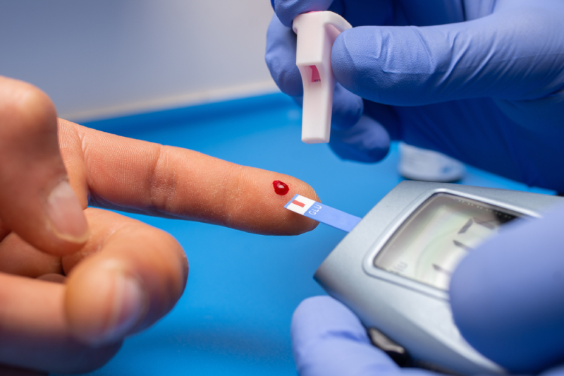 A doctor using a digital glucose monitor and test strip to check a patient's blood sugar level from a finger prick.