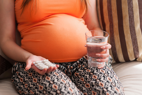 Close-up of a pregnant woman's hand holding folic acid tablets.