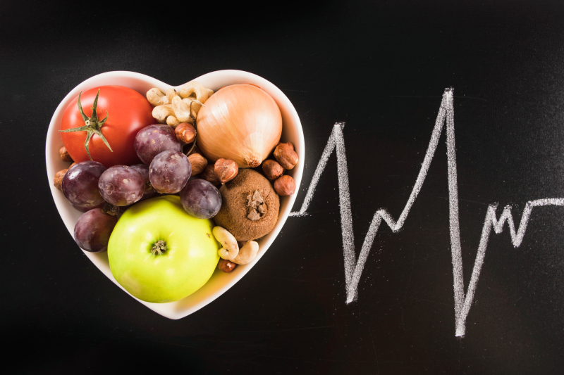 A heart-shaped bowl of fruits, vegetables, and nuts with a heart line, symbolizing nutrition's impact on cardiac health.