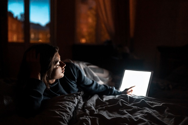 A woman lies in bed at night, using a laptop in a dark room, its screen glowing as it impacts her sleep and blood sugar levels.