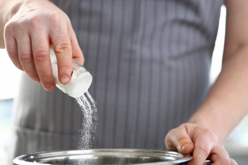 A person pouring salt into a steel bowl, highlighting the connection between high salt intake and high blood pressure.