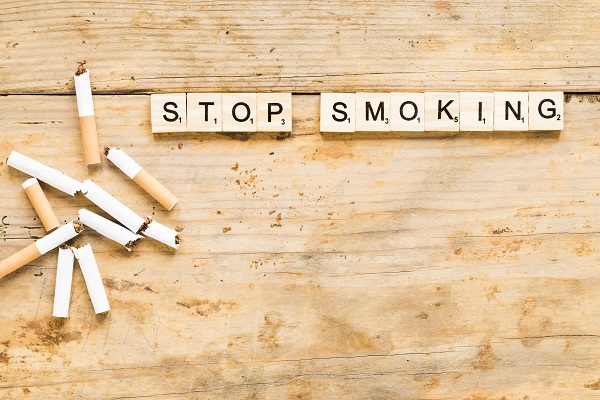 Broken cigarettes on a wooden surface with 'STOP SMOKING' in Scrabble tiles, symbolizing a no-smoking message.