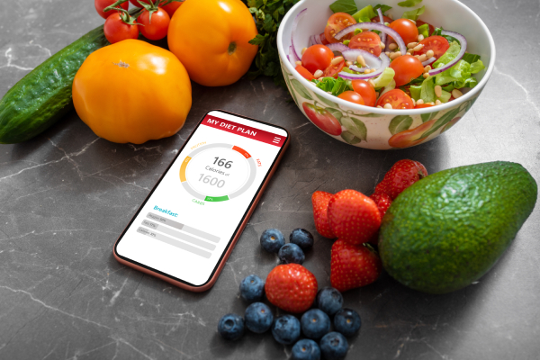 A smartphone displaying a healthy meal planning app on a kitchen counter, surrounded by fresh vegetables and fruits.