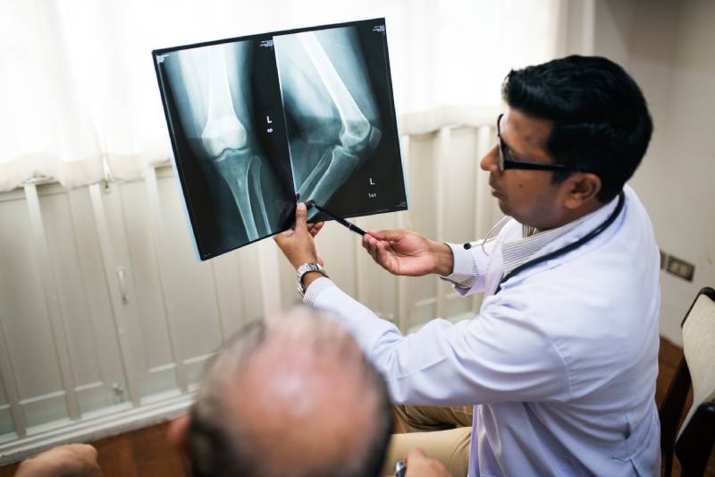 A doctor pointing to an X-ray, explaining how body posture affects bone health, with a bone density scan beneficial for older adults.