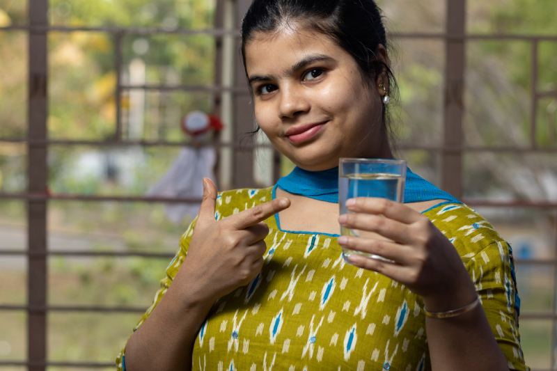 Smiling woman pointing at a glass of water, highlighting hydration.