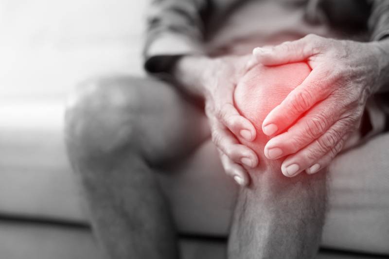 An elderly man holding his painful knee, symbolizing cartilage degeneration caused by arthritis and aging.