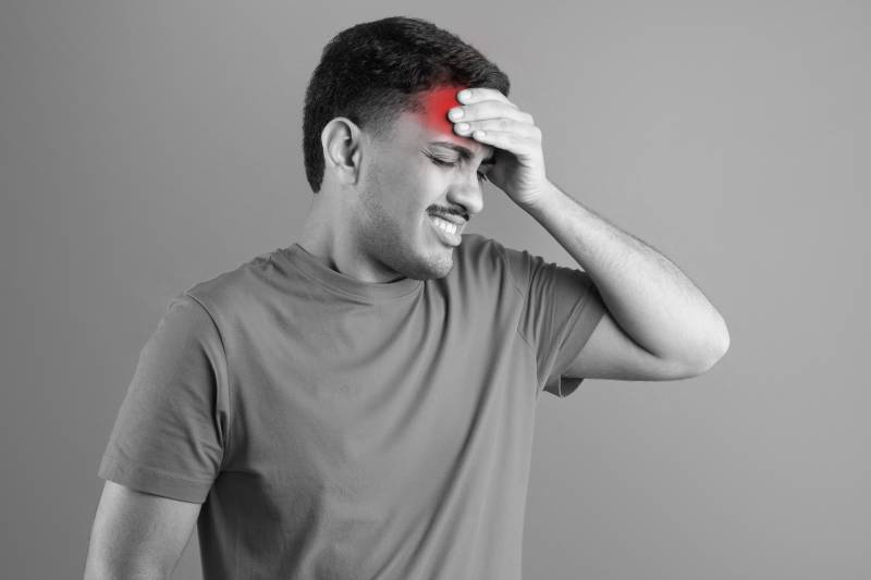 A man in pain holding his forehead, indicating a warning sign of high blood pressure and the importance of monitoring fluctuations.