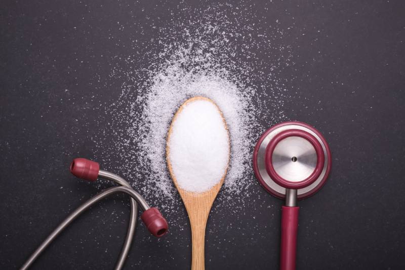 A wooden spoon with salt and a stethoscope, highlighting the impact of excess salt on blood pressure and diet.