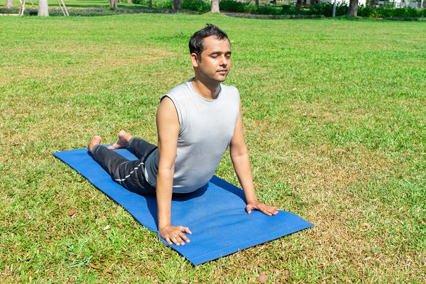 A man practicing yoga outdoors, enhancing body flexibility and reducing stress, which positively impacts blood pressure.