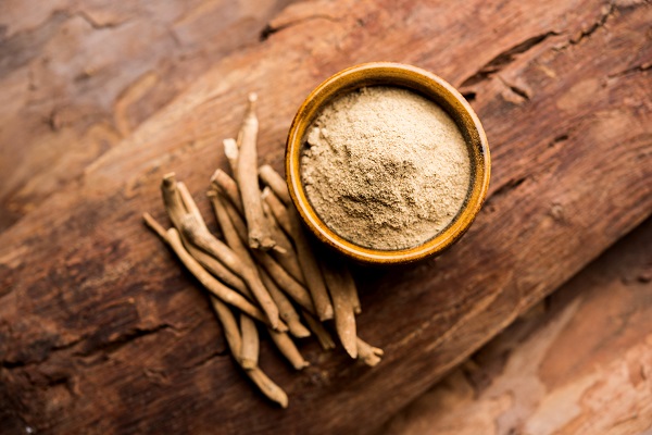 Ashwagandha roots and powder in a bowl on a wooden surface, symbolizing Ayurvedic herbs.