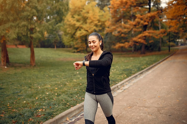 A woman in sportswear walking in a park and checking her smartwatch, symbolizing the health benefits of brisk walking.