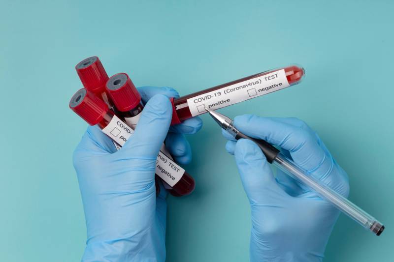 A person marking a Covid blood test tube with a pen to indicate a positive result, showing how blood tests assist in treatment and monitoring.