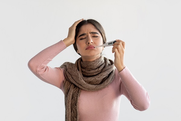A woman with a headache using a thermometer, suggesting serious brain or spinal cord inflammation needing urgent care.