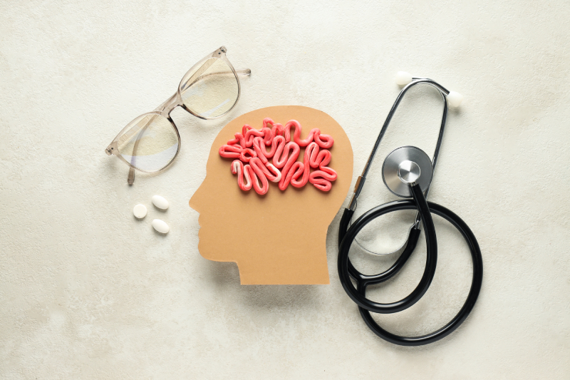 A cardboard head with brain-shaped intestines, glasses, and pills symbolizes Parkinson’s impact on memory, mood, and sleep.