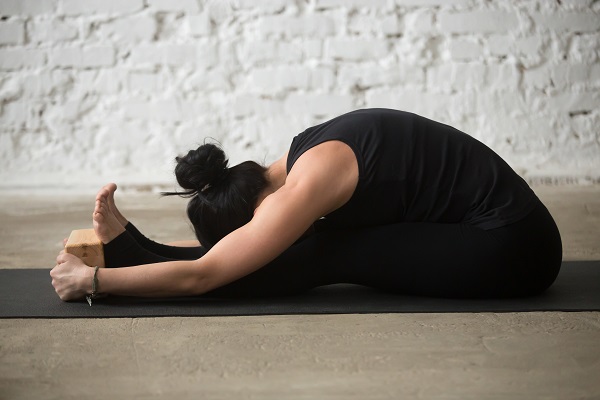 A woman practicing Paschimottanasana, a seated forward bend yoga pose.
