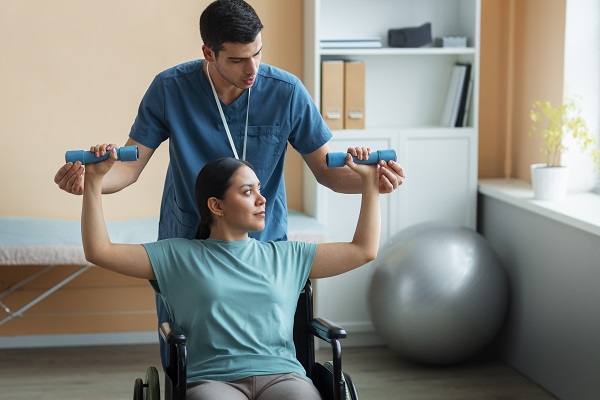 A physician rehabilitates a patient in a wheelchair lifting dumbbells.