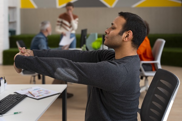 A worker stretching at a desk to relieve muscle tension, highlighting the importance of regular breaks.