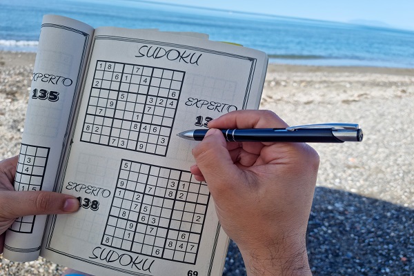 A person solving sudoku at the beach, symbolizing brain exercises that support cognitive health.