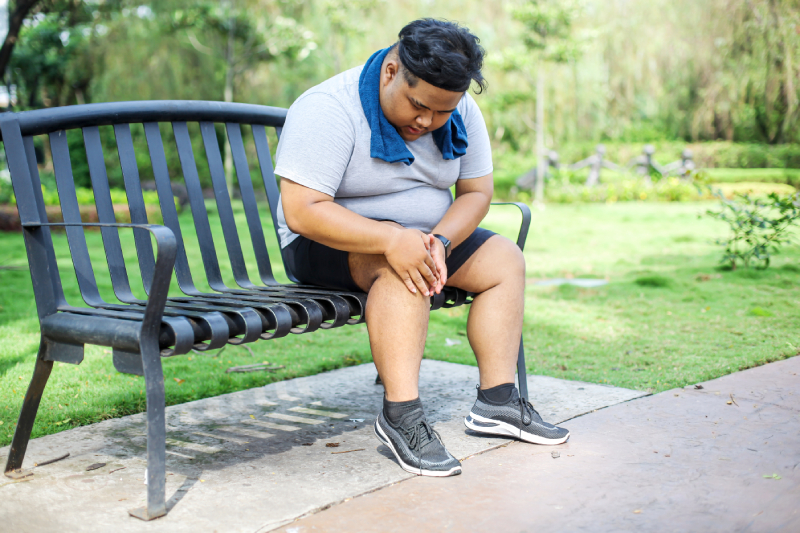 An overweight man grips his knee in pain post-workout, showing the link between obesity and arthritis.