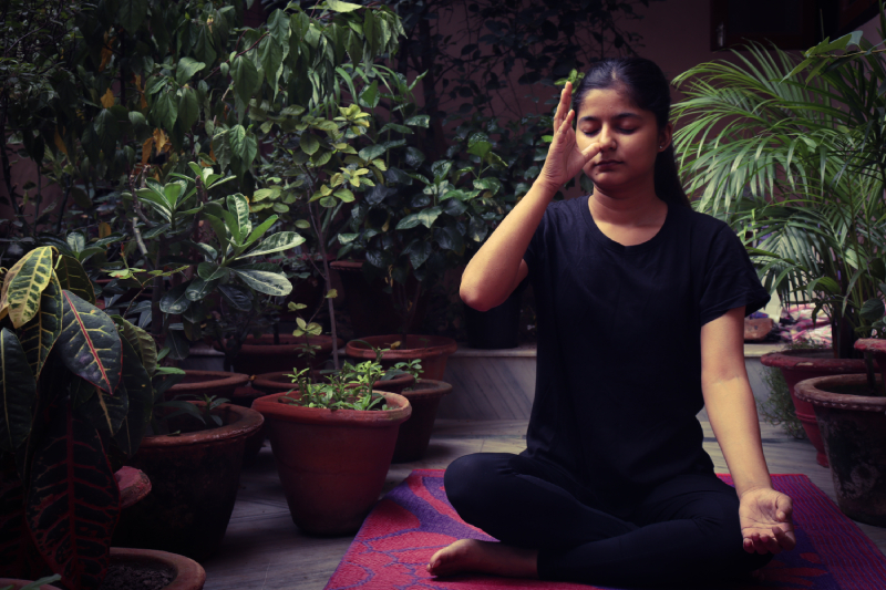 A woman practicing yoga and breathing exercises in a peaceful garden, representing how yoga boosts creativity.