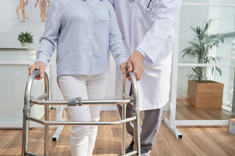A rehabilitation specialist helps a patient practice walking with a walker.