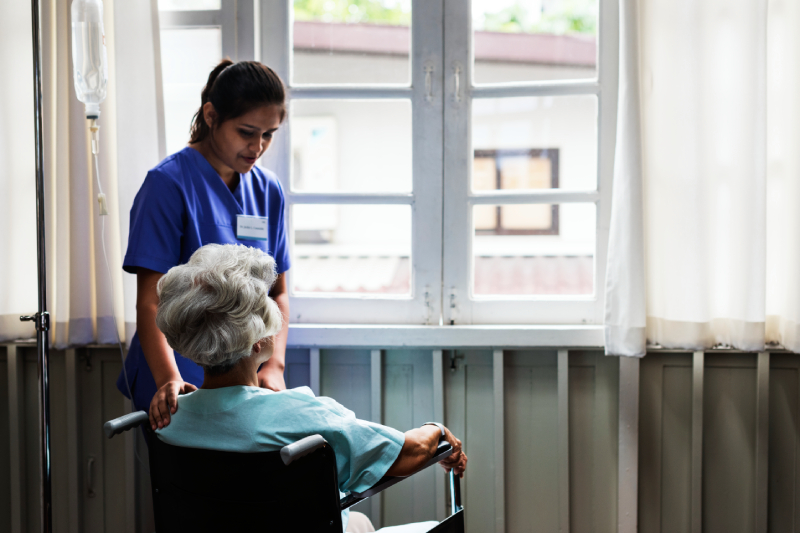 Elderly woman in wheelchair with caregiver shows importance of trained Parkinson’s care.