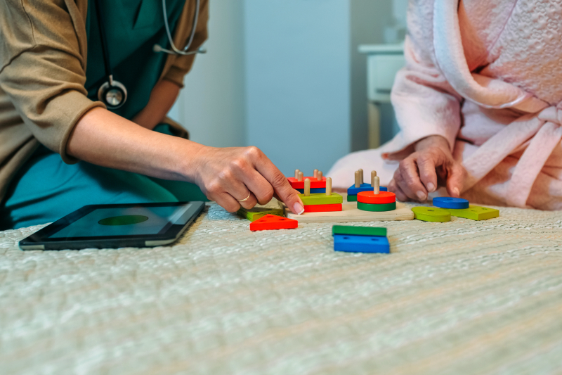 A professional assisting an elderly Parkinson’s patient with wooden puzzles to enhance motor skills and body movements.
