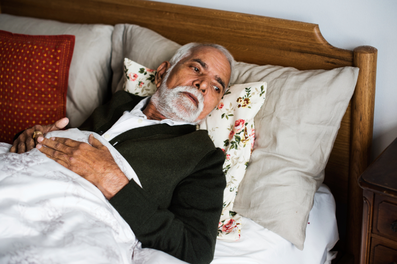 An elderly man in bed experiencing sleep disturbances caused by Parkinson’s disease.