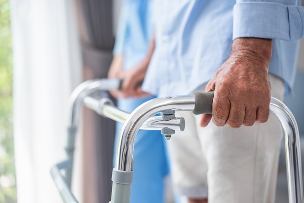 An elderly person using a walker for support receives assistance with tailored exercises for Parkinson’s disease. 